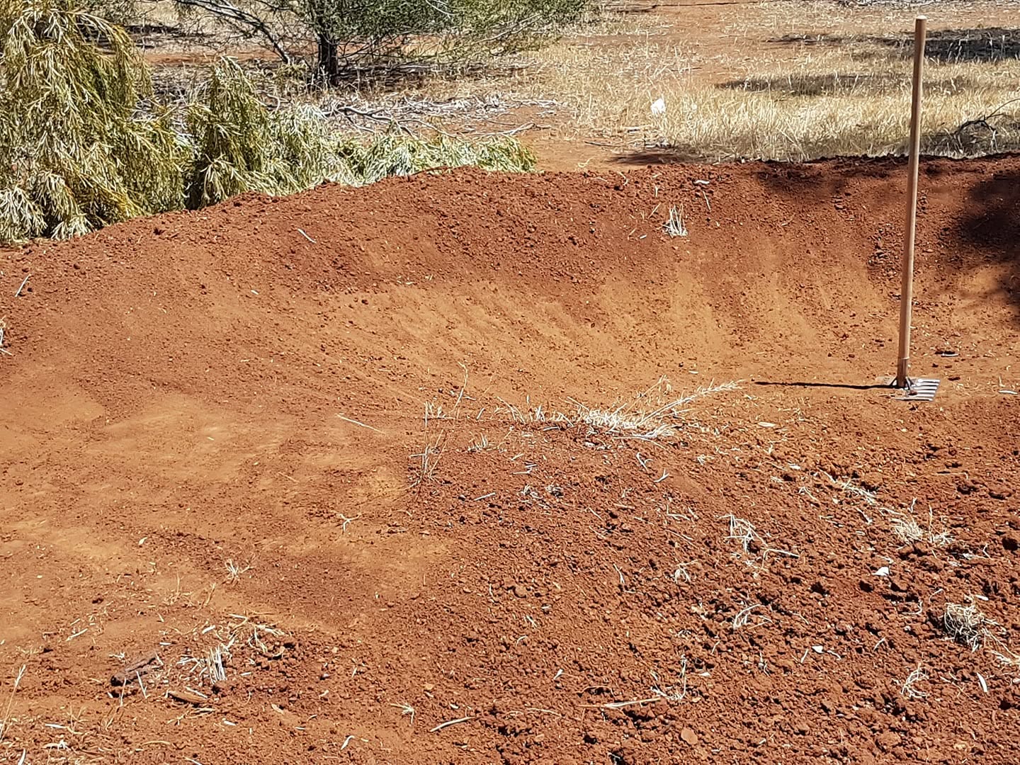 Freshly shaped red dirt berm beside dry grass and low shrubs