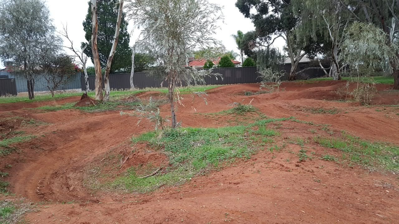 Curved red dirt track corner with a boundary fence and eucalypts behind