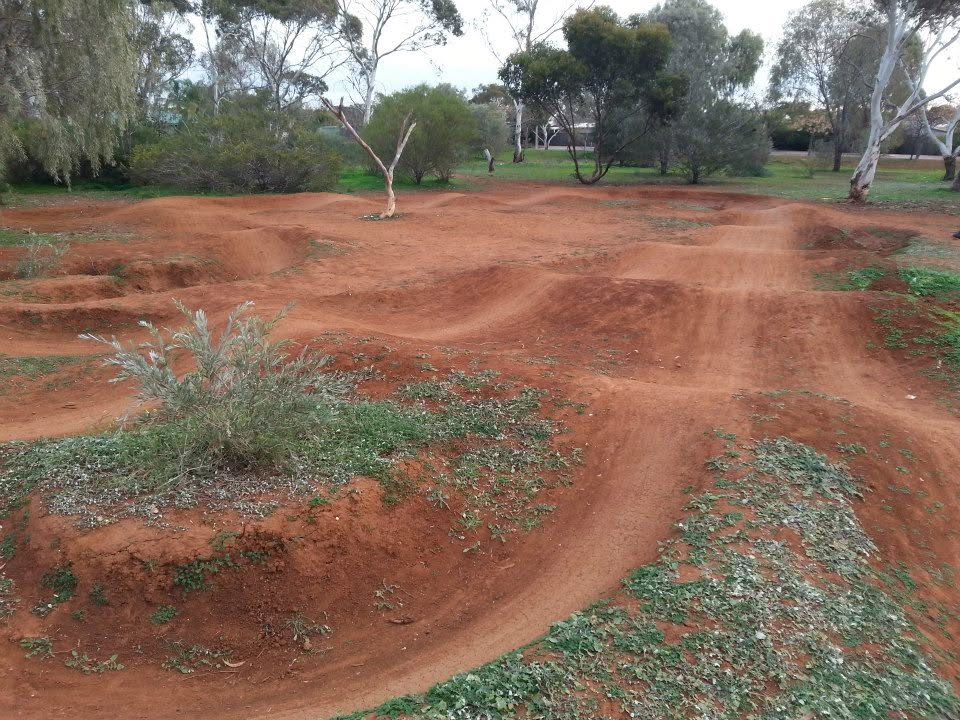 Red dirt rollers and berms with green plants and gum trees in the background